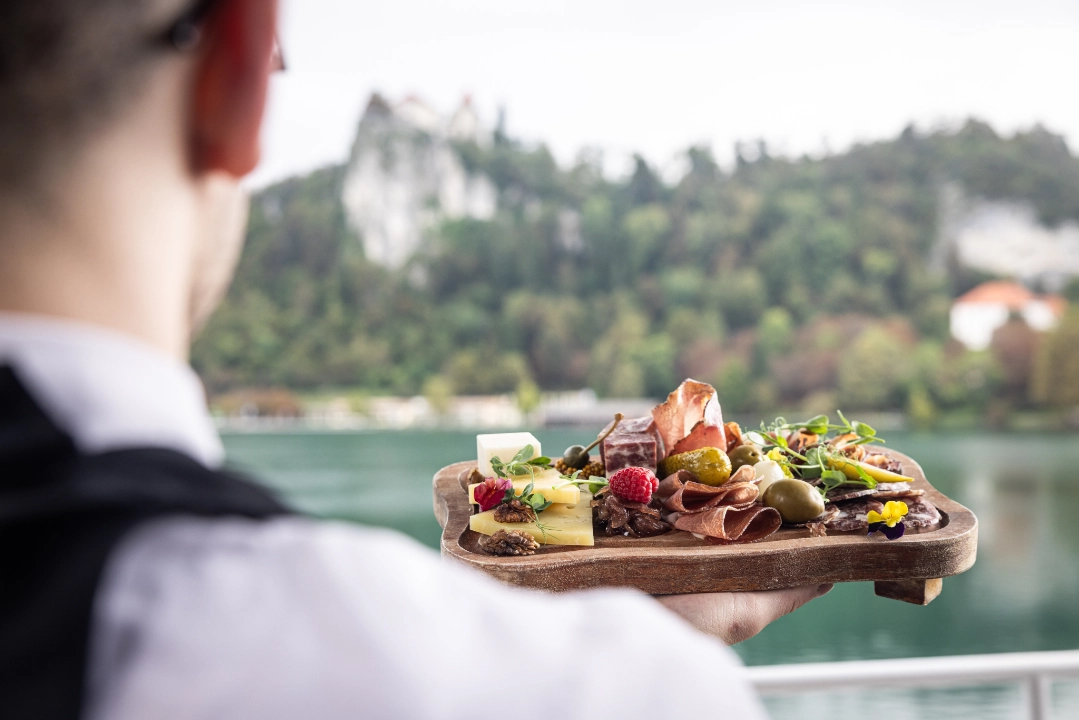 A chef holding a slovenian traditional cold starter dish facing the lake Bled in the background.