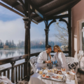 Pair is eating breakfast on the terrace with misty lake in the background