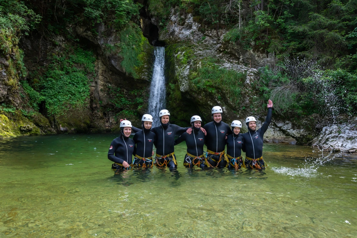 Group of people standing in the water in full safety gear with waterfall behind them