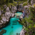 Person is climbing on a rocks with emerald water gorge under