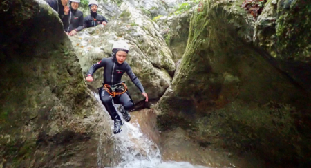 Boy jumps to the river from rocks in a full safety gear