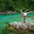 Women is stretching on a rock with emerald river in the background