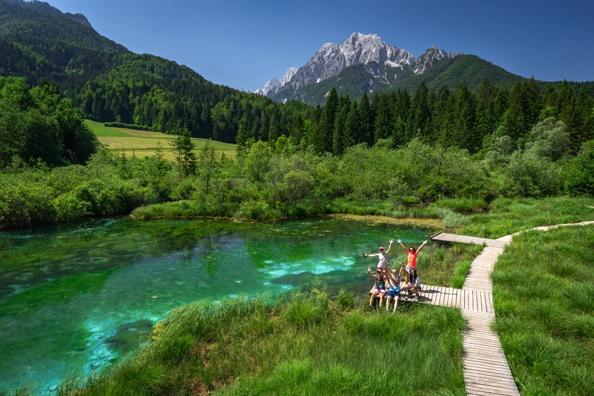 Group of people is waving and smiling while standing on wooden terrace in mountain scenery