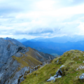 Mountain ridge with grassy terrain and rocky slopes, surrounded by misty blue mountains in the distance.