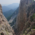Narrow rocky gorge between towering cliffs with distant mountain scenery beyond.