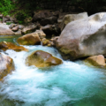 Clear mountain stream flowing over smooth rocks, creating turquoise pools and small rapids.