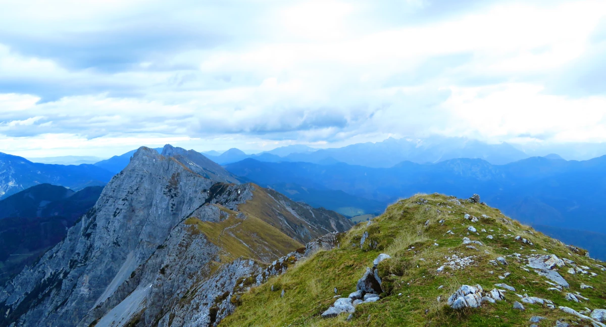 Mountain ridge with grassy terrain and rocky slopes, surrounded by misty blue mountains in the distance.