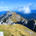 Panoramic view of mountain peaks under a blue sky with clouds, taken from a hiking trail.