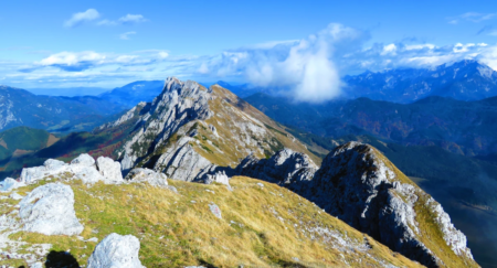 Panoramic view of mountain peaks under a blue sky with clouds, taken from a hiking trail.